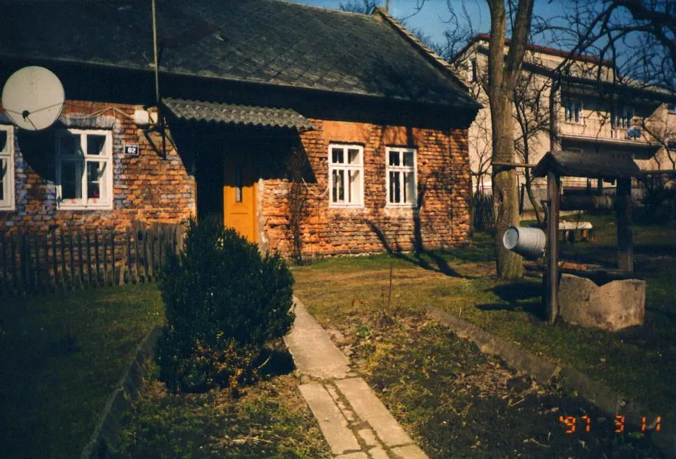 Stary murowany dom kryty dachówką, otoczony drzewami.