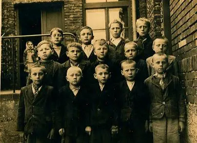 Czarno-białe zdjęcie grupy dzieci przed murowanym budynkiem szkoły.