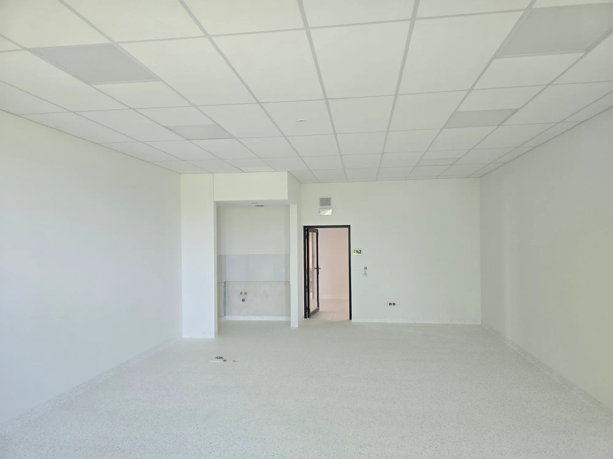Pusta sala lekcyjna z białymi ścianami i sufitem podwieszanym.