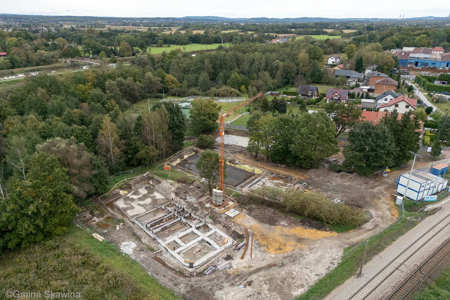 Plac budowy z żurawiem wieżowym i siatką odsłoniętych fundamentów.