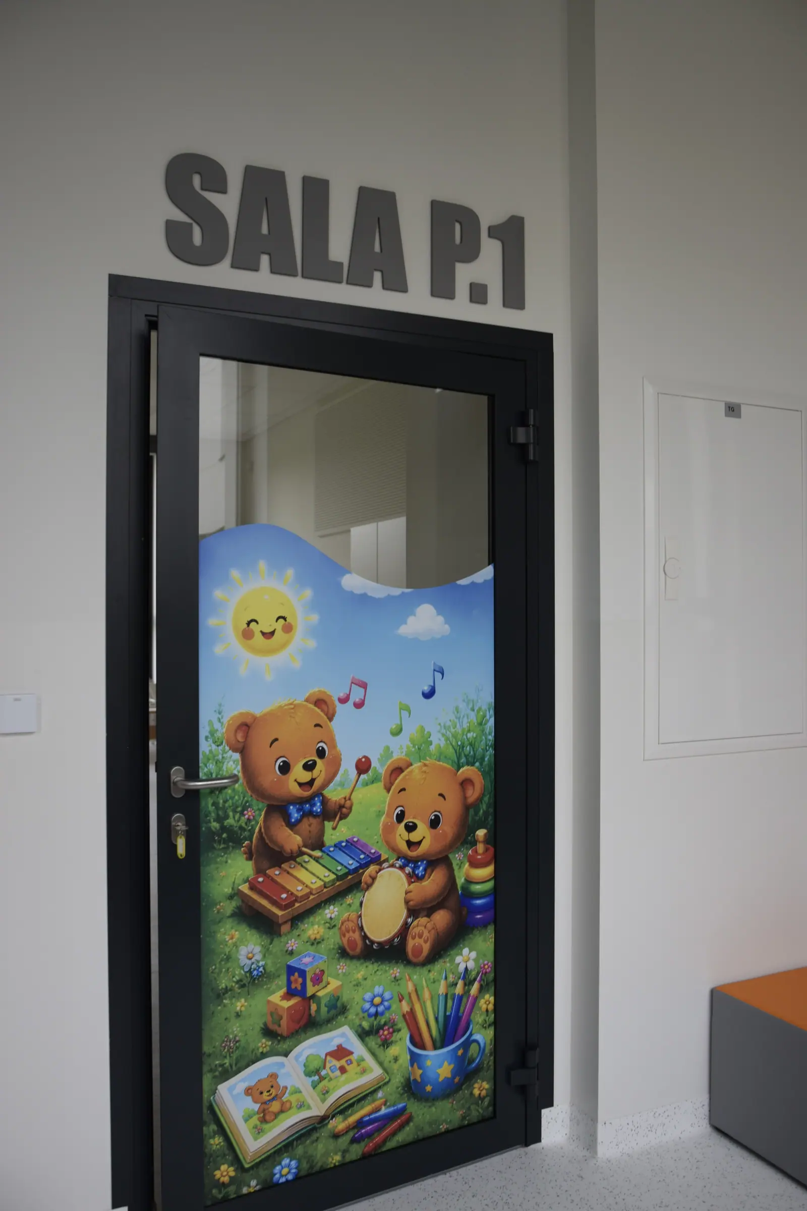 Otwarte drzwi sali przedszkolnej z kolorową ilustracją misiów, nad nimi napis SALA P.1.